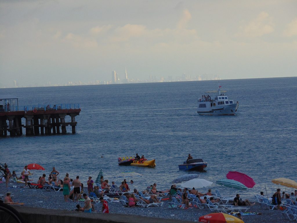Beachgoers and boats off Kobuleti, with the Batumi skyline beyond, mark the town’s festive seaside atmosphere.