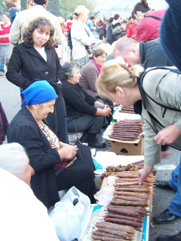 Vendors and visitors gather around a churchkhela stall at a Georgian wine festival.