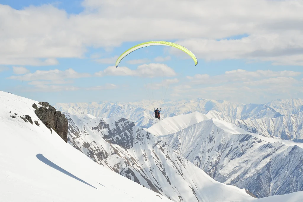 A solo paraglider glides over the snow-covered ridges surrounding Gudauri.