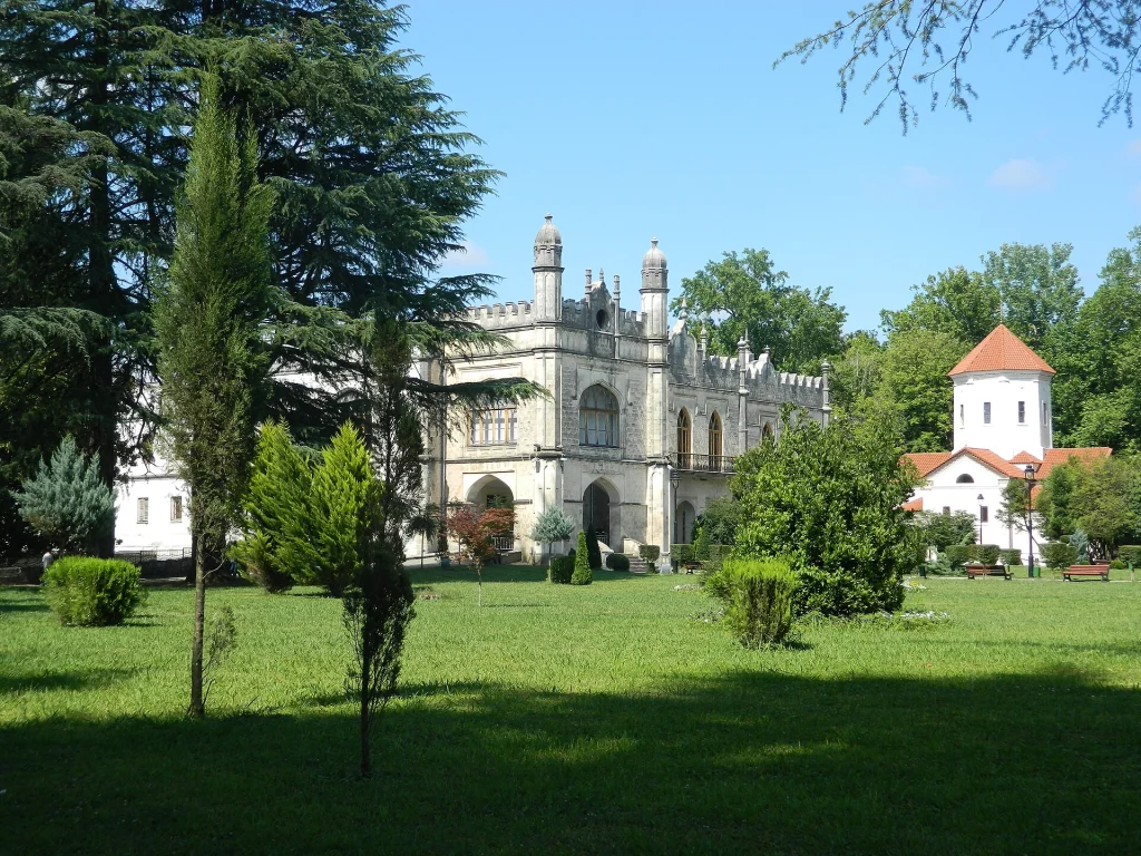 The Gothic-style Dadiani Palace in Zugdidi seen across a green lawn with trees.