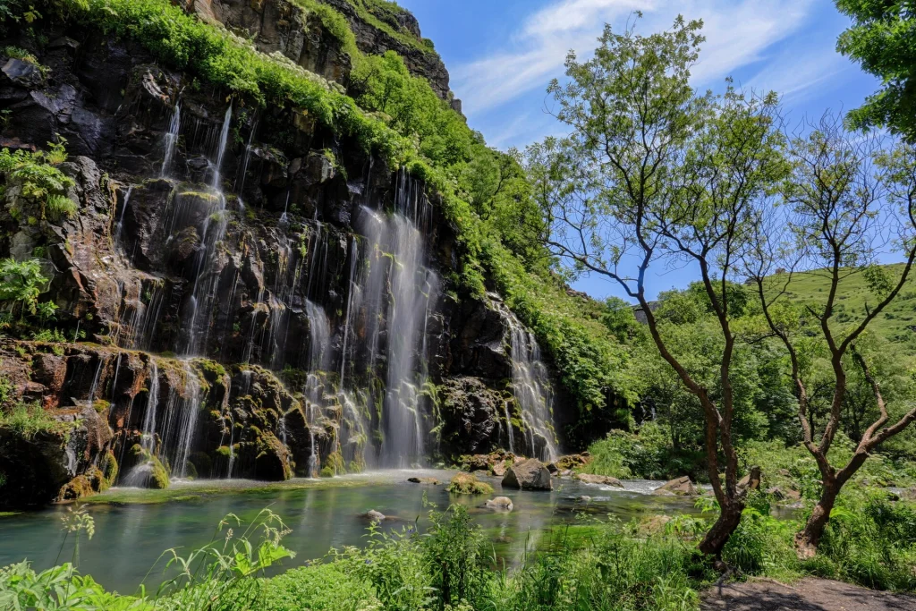 Dashbashi Canyon waterfall surrounded by lush green vegetation under a blue sky.