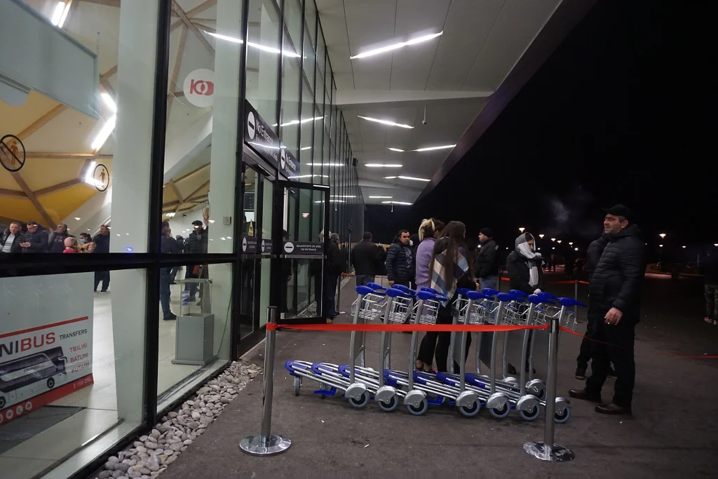 Night-time transfer buses and passengers outside Kutaisi International Airport terminal.