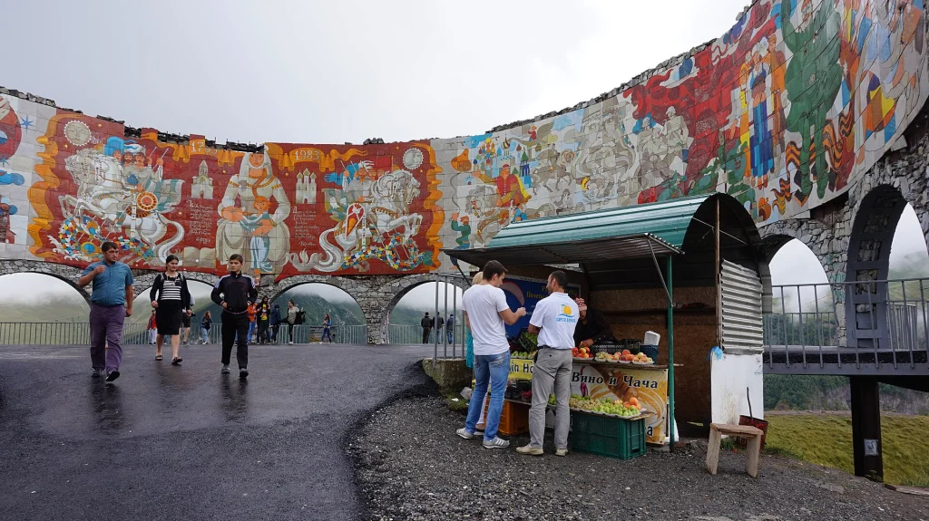 A fruit stall does business beside the mural wall, a popular stop for travelers on the road.
