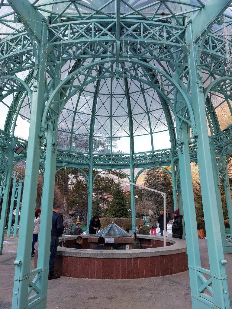 Visitors gather around the historic Ekaterine Well mineral spring inside its ornate ironwork pavilion.