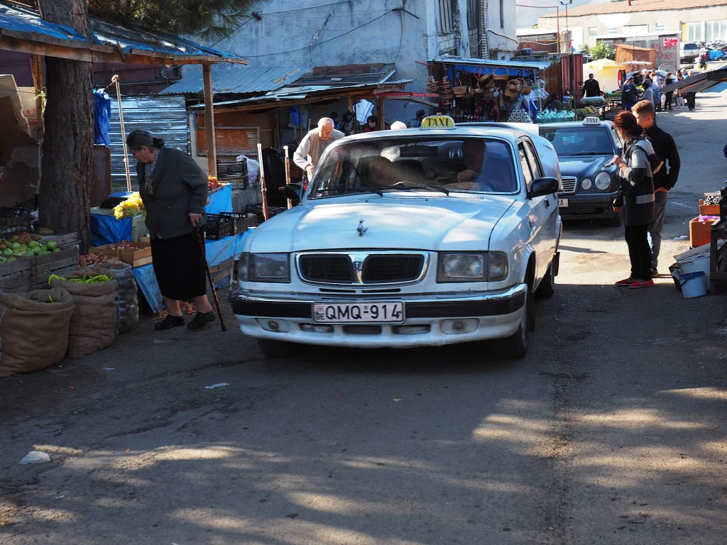 A taxi waits by a Tbilisi street market, reflecting local taxi services where tipping customs vary.