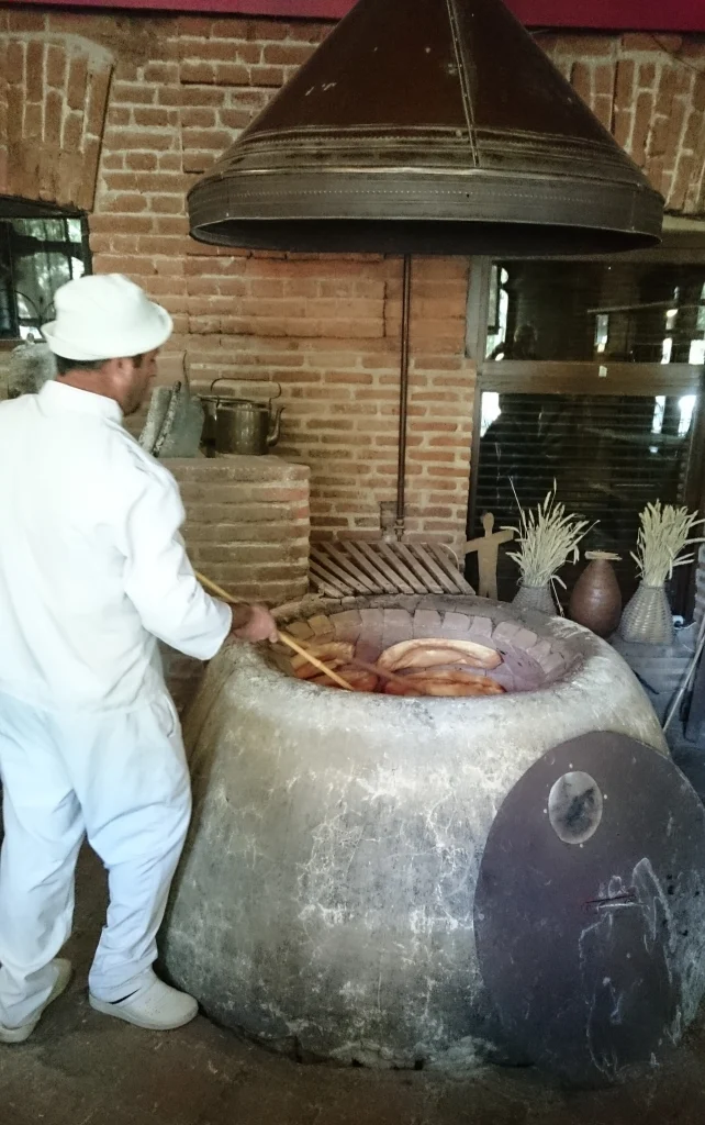 A chef bakes traditional flatbread in a clay tone oven at a Georgian restaurant.