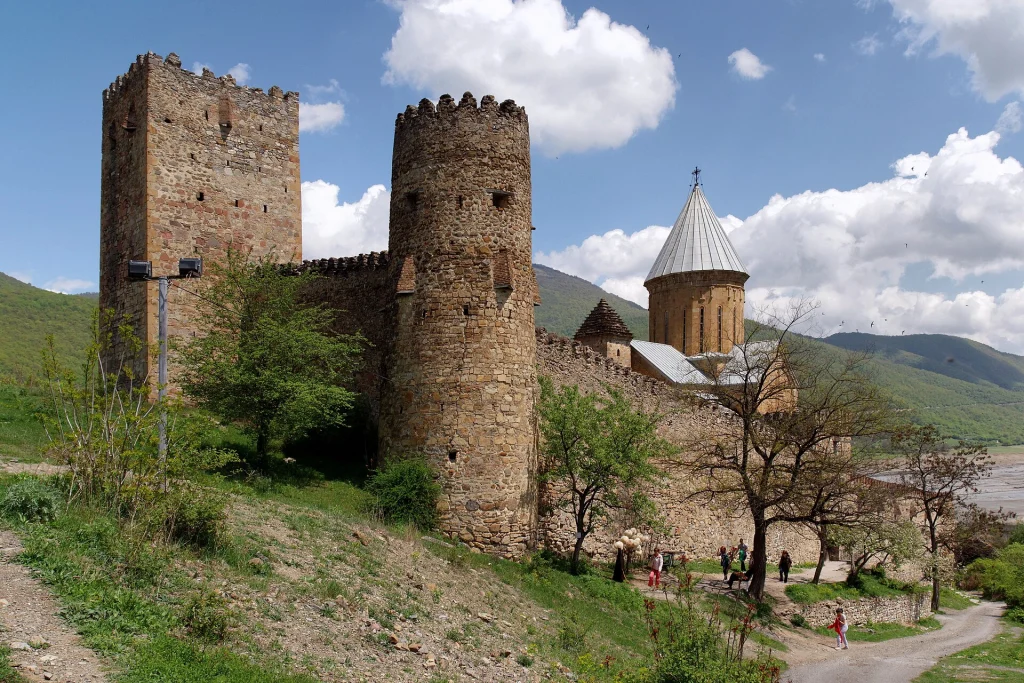 Visitors walk among the stone towers and church of Ananuri fortress complex.