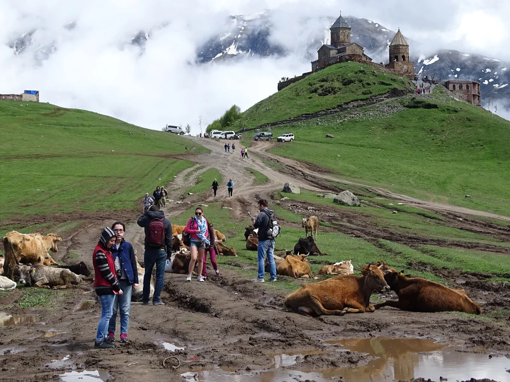 Visitors hike the muddy trail up to Gergeti Trinity Church near Kazbegi, a popular day trip from Tbilisi.