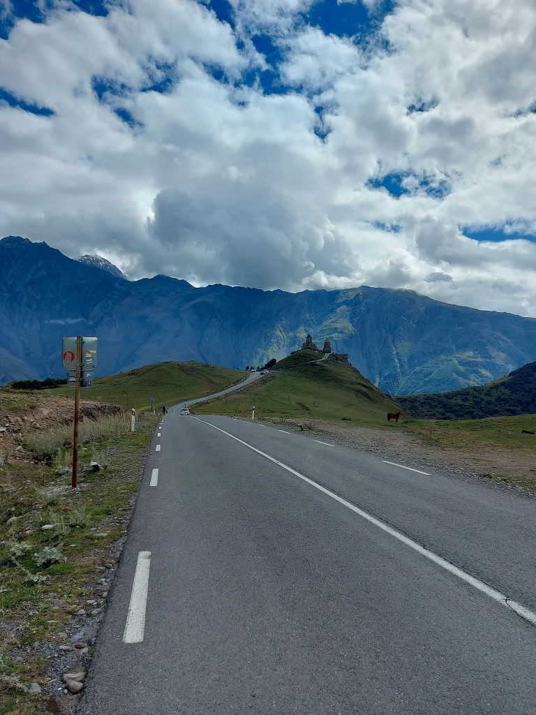 The road toward Kazbegi winds through the mountains with Gergeti Trinity Church visible on its hill.