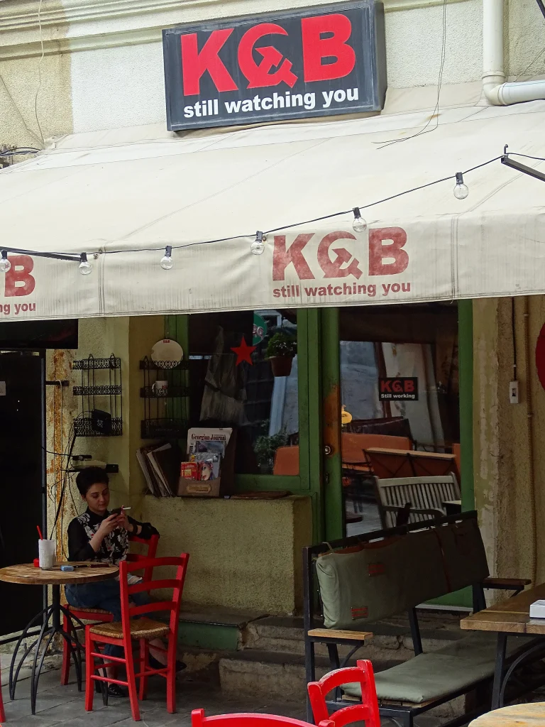 A woman works on her phone at an outdoor café table in Tbilisi's old town.