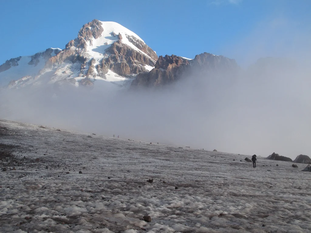 A trekker approaches Mount Kazbek with the Gergeti Glacier's icy terrain underfoot.