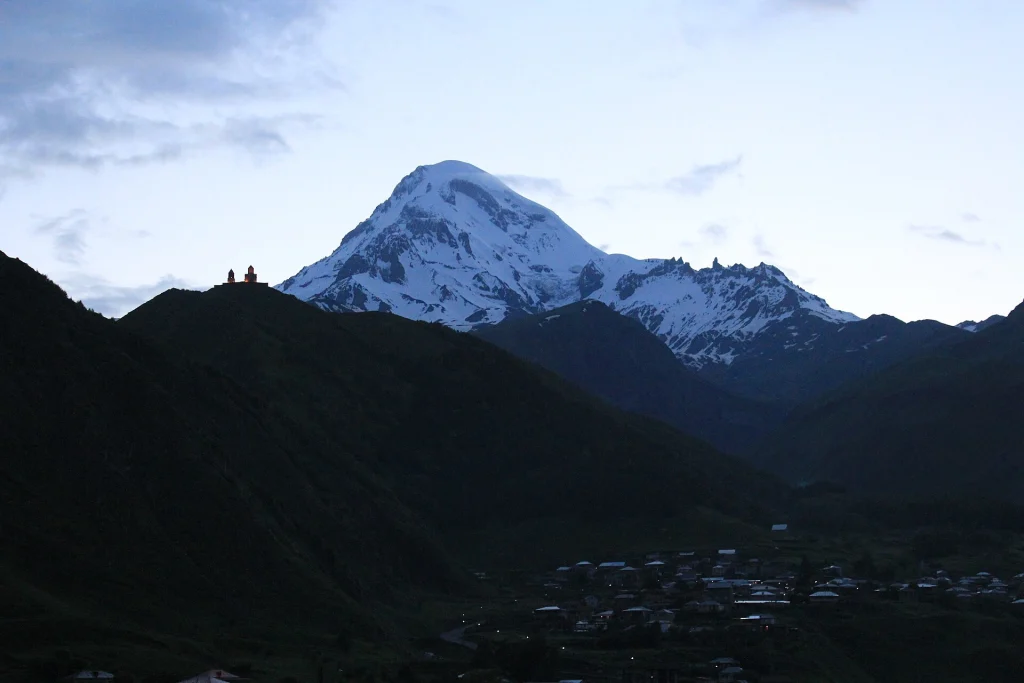 Snow-capped Mount Kazbek towering over the village, showing Georgia's dramatic Caucasus landscape.