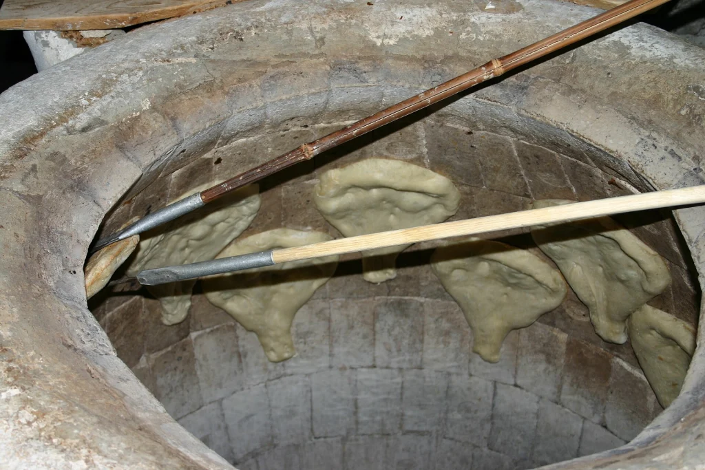 Flatbread dough being placed inside a traditional clay tone oven in Georgia.
