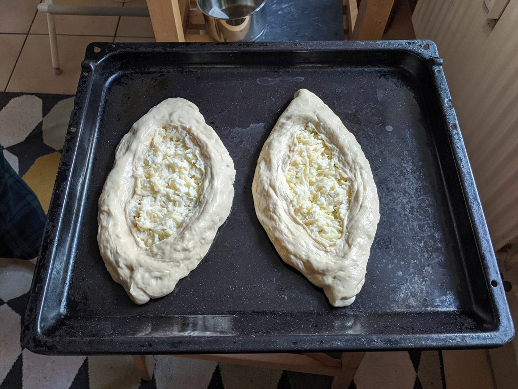 Two Adjarian khachapuri being prepared and filled with cheese before baking, illustrating the craft behind the national dish.