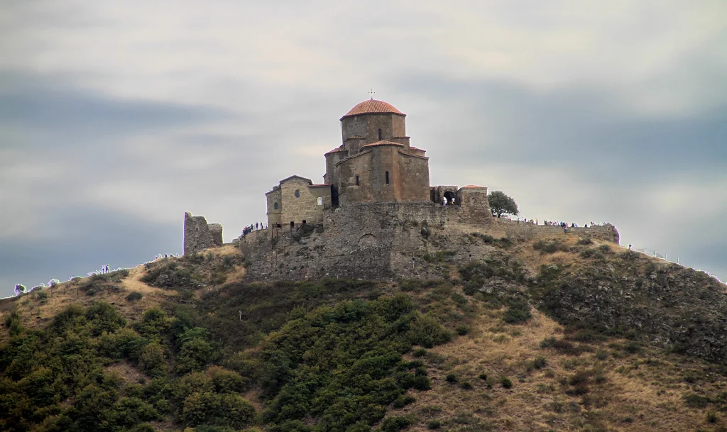 Jvari Monastery church crowning a hilltop above Mtskheta under a cloudy sky.