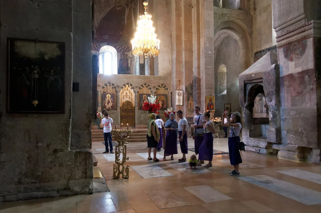 Visitors with candles stand inside the illuminated nave of Svetitskhoveli Cathedral.