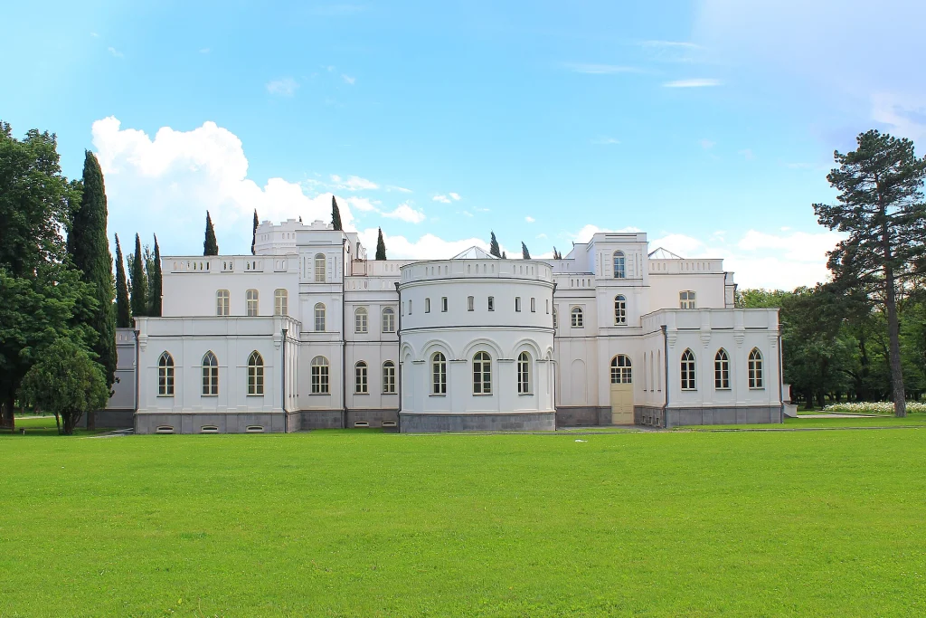 Wide view of Château Mukhrani's white facade surrounded by cypress trees and lawn.