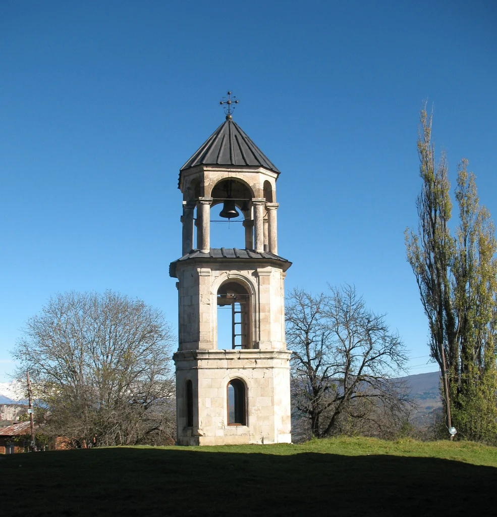 The bell tower of Nikortsminda Cathedral in Racha, Georgia, surrounded by autumn trees.