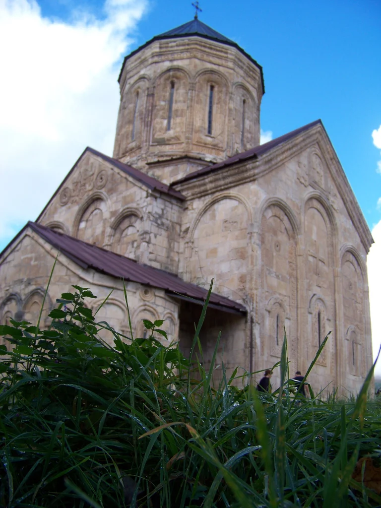 The medieval Nikortsminda church in Racha, Georgia, viewed from below against a blue sky.