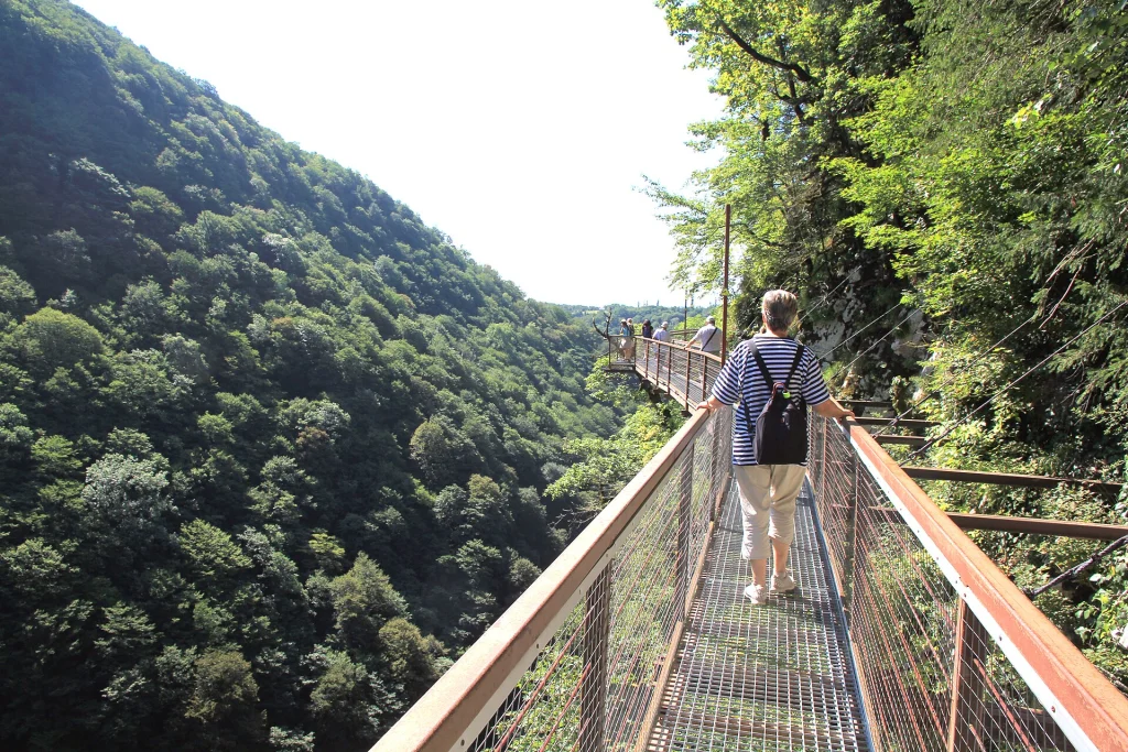 A visitor walks the suspended metal walkway through Okatse Canyon's steep gorge.
