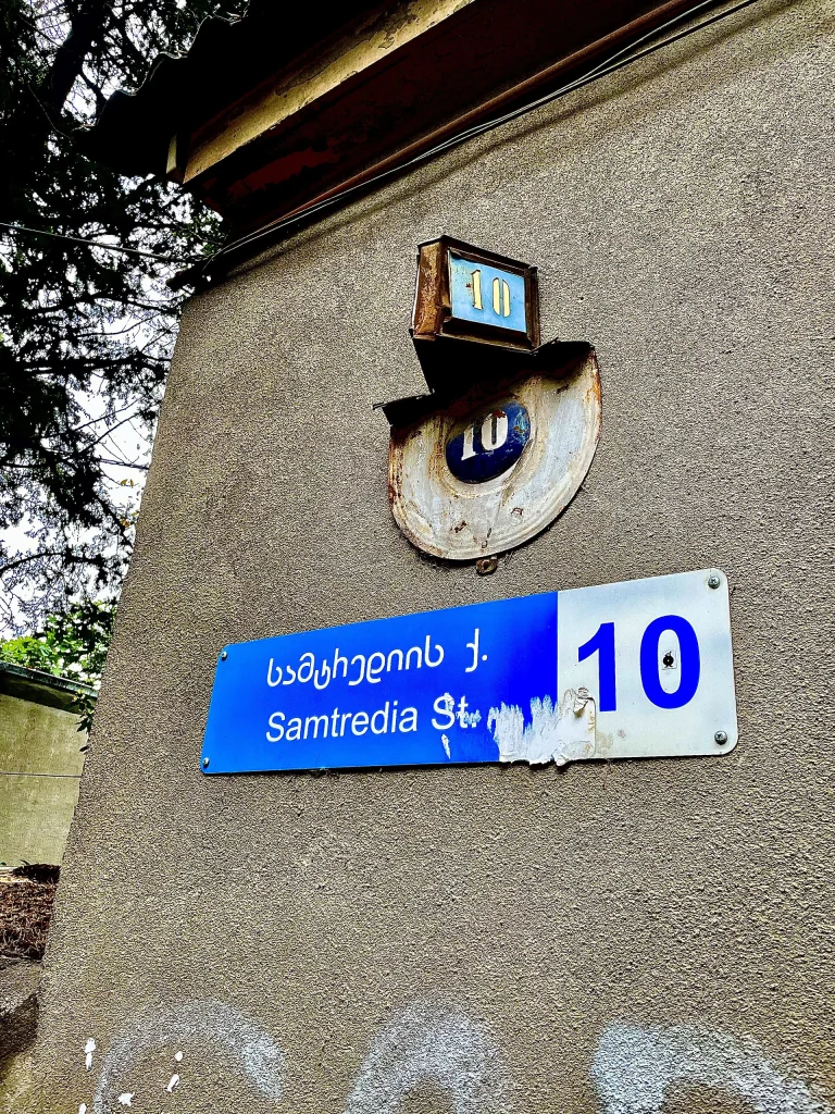 Old and new street signage on Samtredia Street in Tbilisi shows Georgian lettering alongside numerals and Latin script.