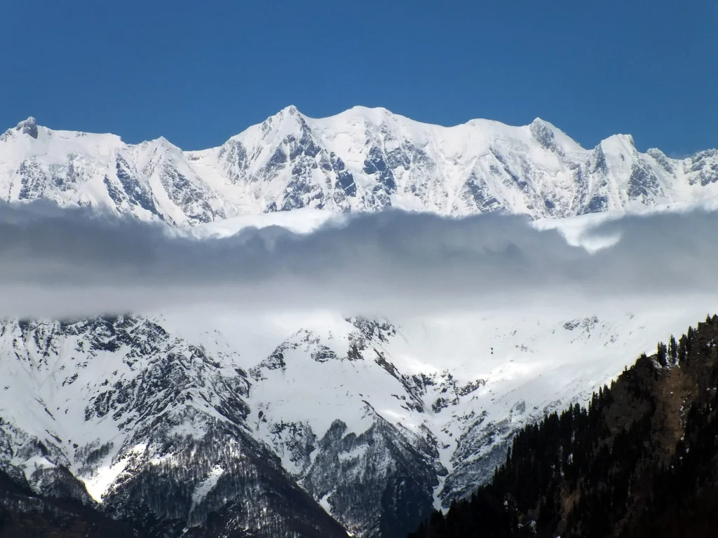 A dramatic snow-covered mountain ridge in Svaneti emerges above low clouds.