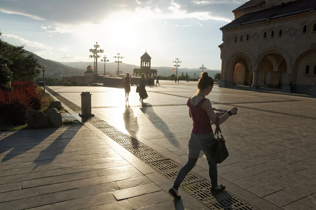 Tourists walk through the sunlit square beside Sameba Cathedral in Tbilisi.