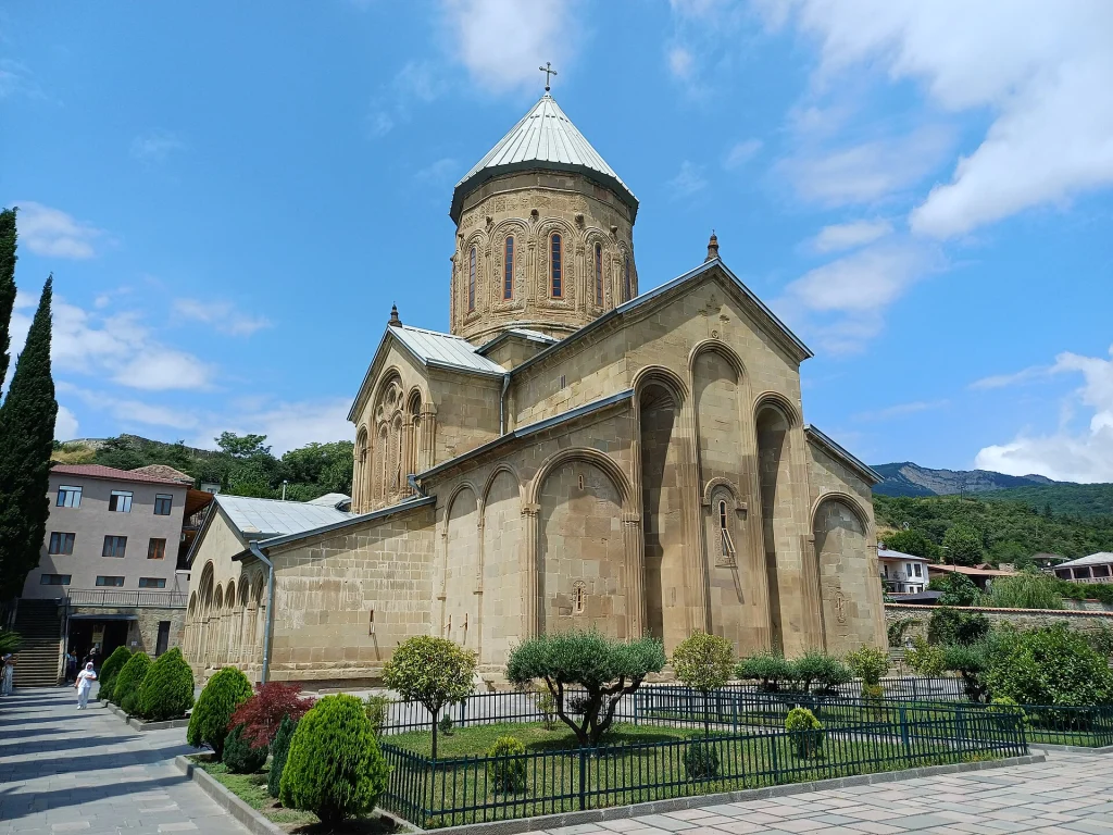 Samtavro Monastery church with its domed tower set against a blue sky and gardens.