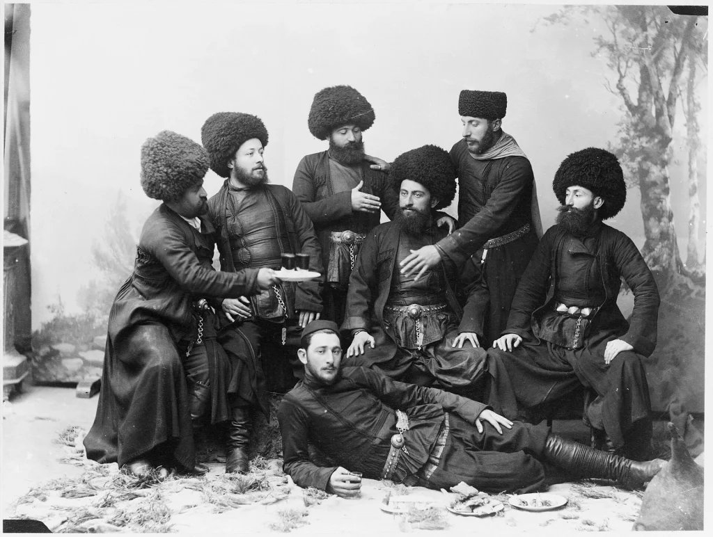 Men in traditional Caucasian dress pose around a feast spread, evoking the Georgian supra.