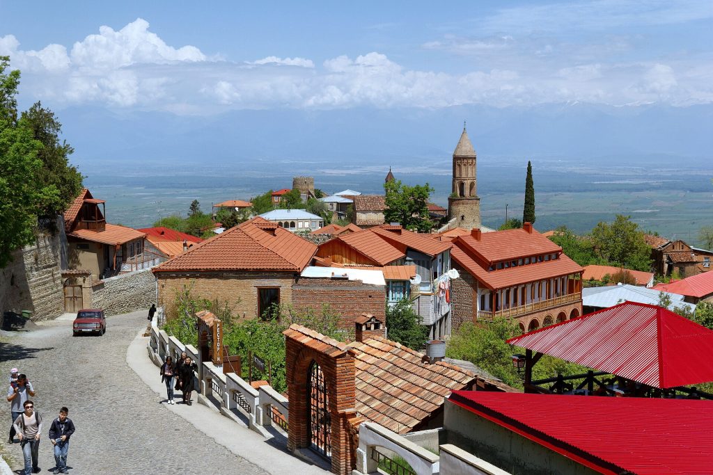 A view down a Sighnaghi street with red-tiled roofs and visitors strolling near the town center.