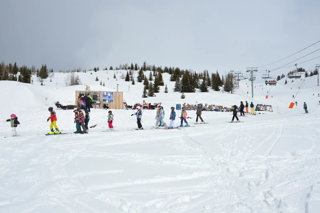 Young ski-school pupils practising turns in front of a resort chalet, illustrating kids' lessons.