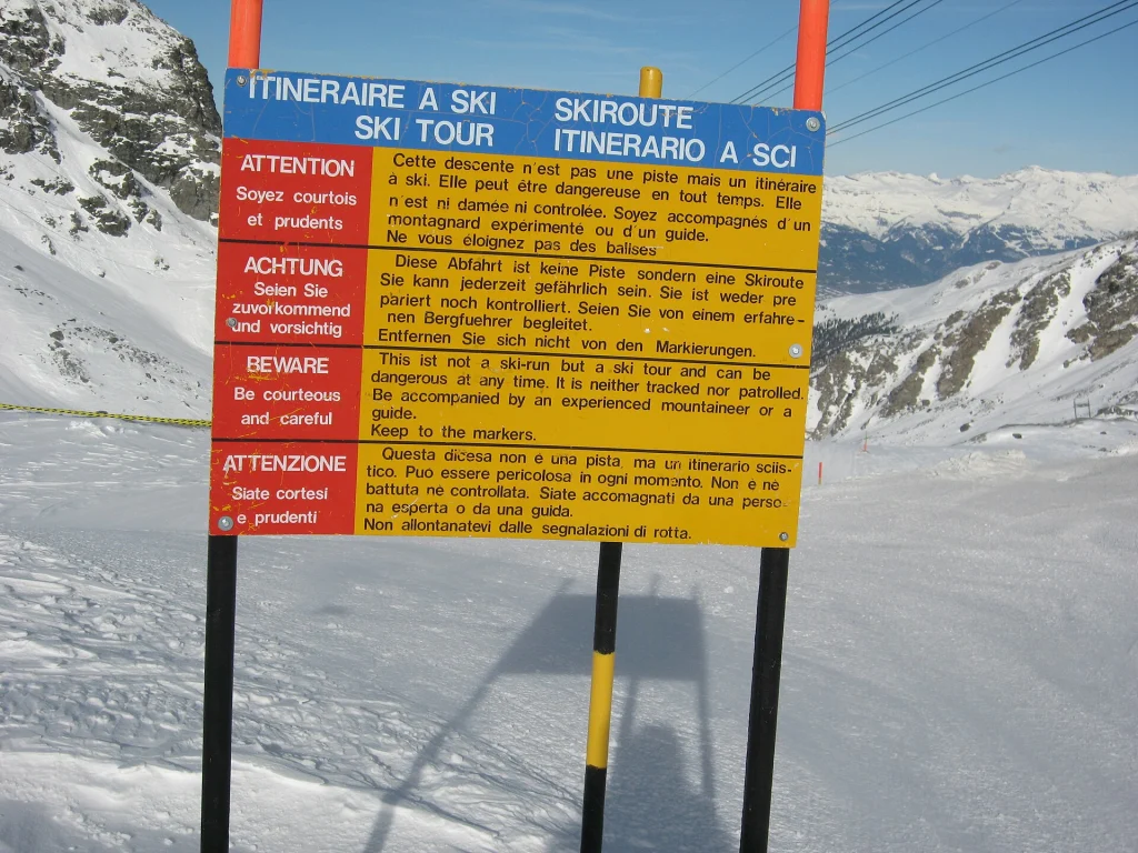 A multilingual ski-tour warning sign reminds backcountry skiers of avalanche and route risks.
