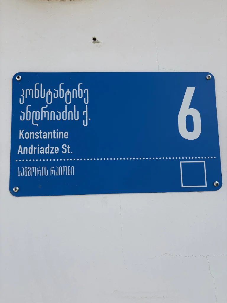 A modern bilingual Tbilisi street sign pairs Georgian script with its English transliteration, 'Konstantine Andriadze St.'