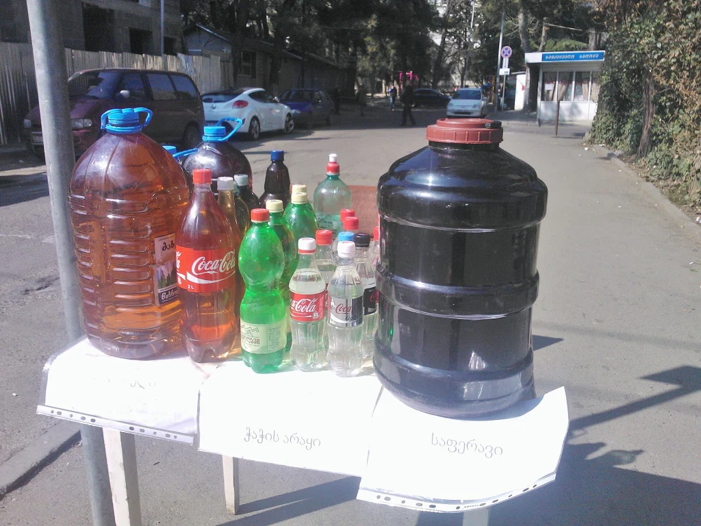 A street vendor in Tbilisi sells homemade wine and chacha from large containers.
