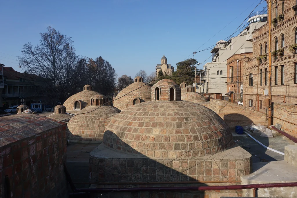 Daylight view of the domed sulphur bathhouses with Tbilisi's old town skyline behind.