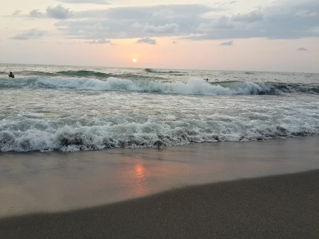 Waves roll onto the dark sand beach of Ureki at sunset.