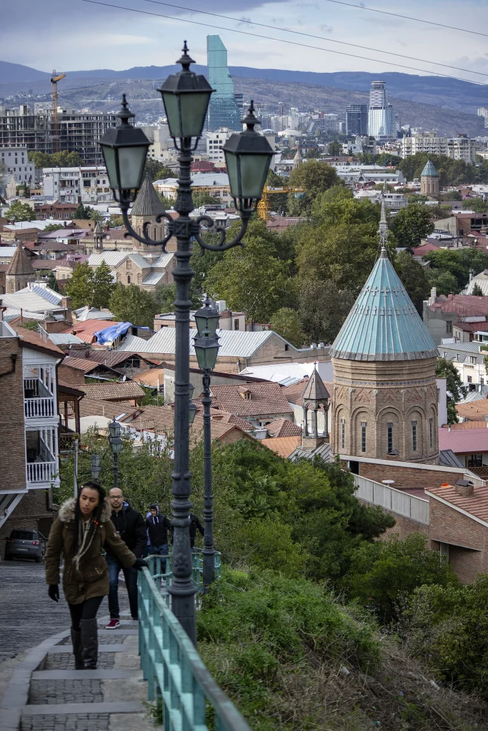 Tbilisi street scene with old town rooftops and modern skyline in the background.
