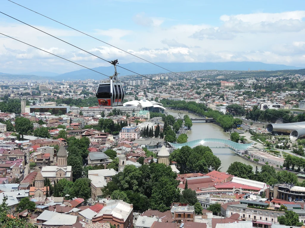 A cable car glides above Tbilisi's Old Town with the river and cityscape below.