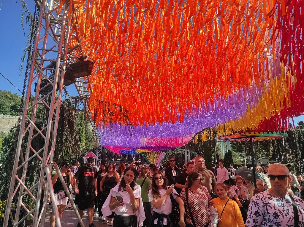 Crowds stroll beneath colourful ribbon canopies at the Tbilisoba festival in Rike park.