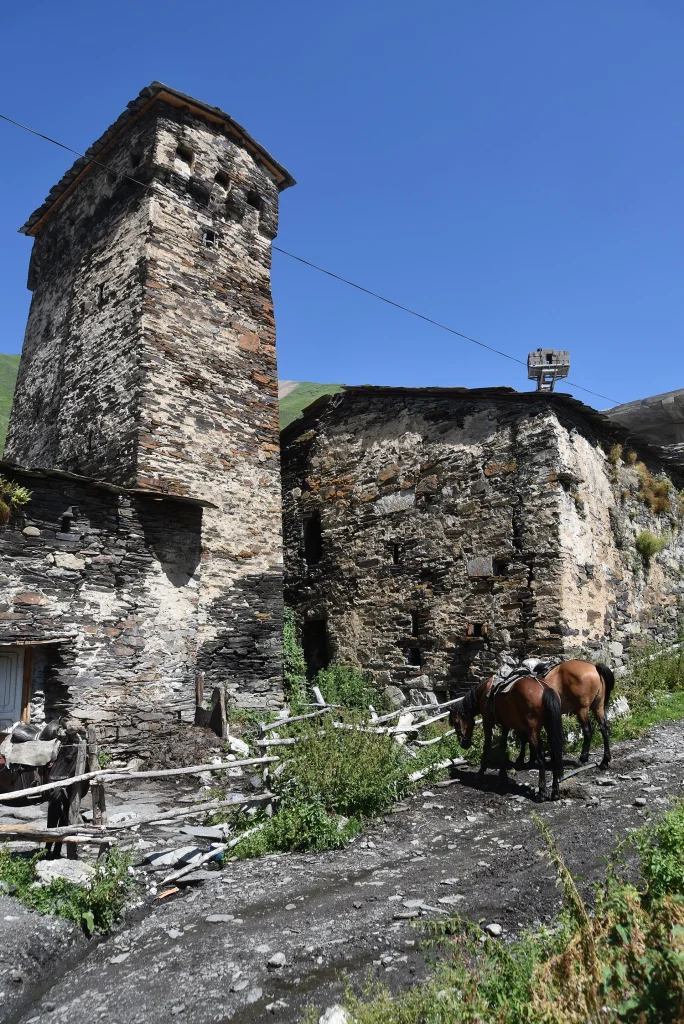 Ancient stone defensive tower and houses of Ushguli village with horses on the road.