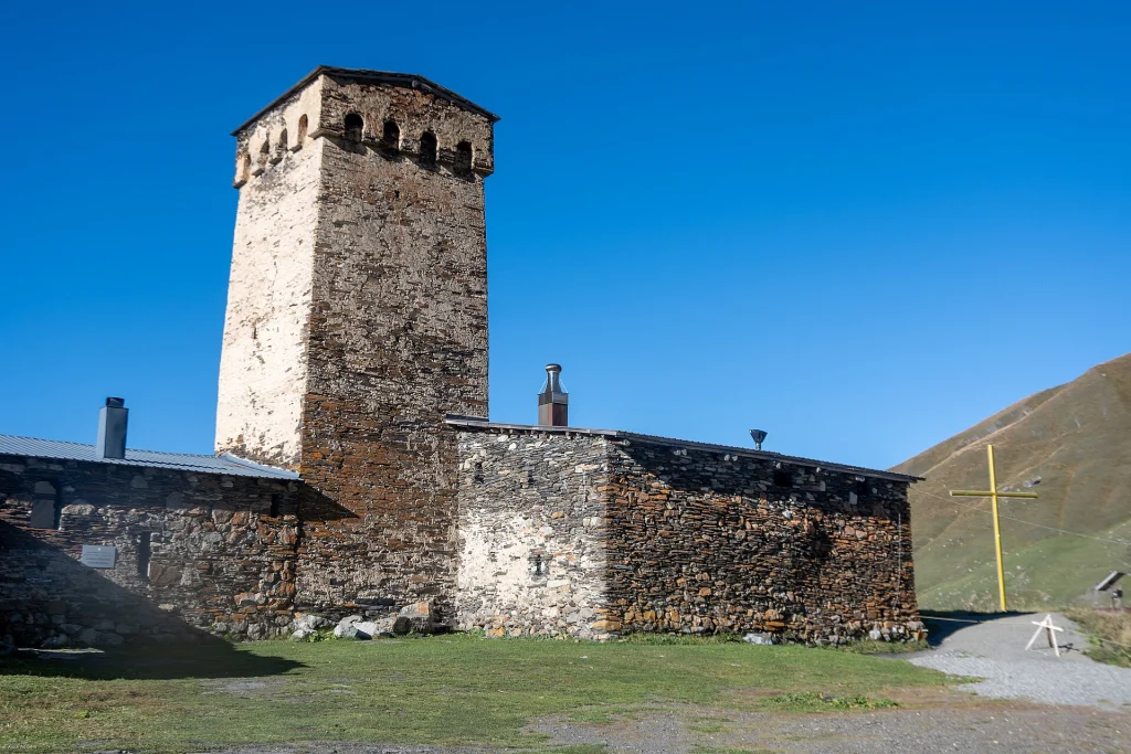 A traditional stone Svan tower in Ushguli stands against a clear blue sky.