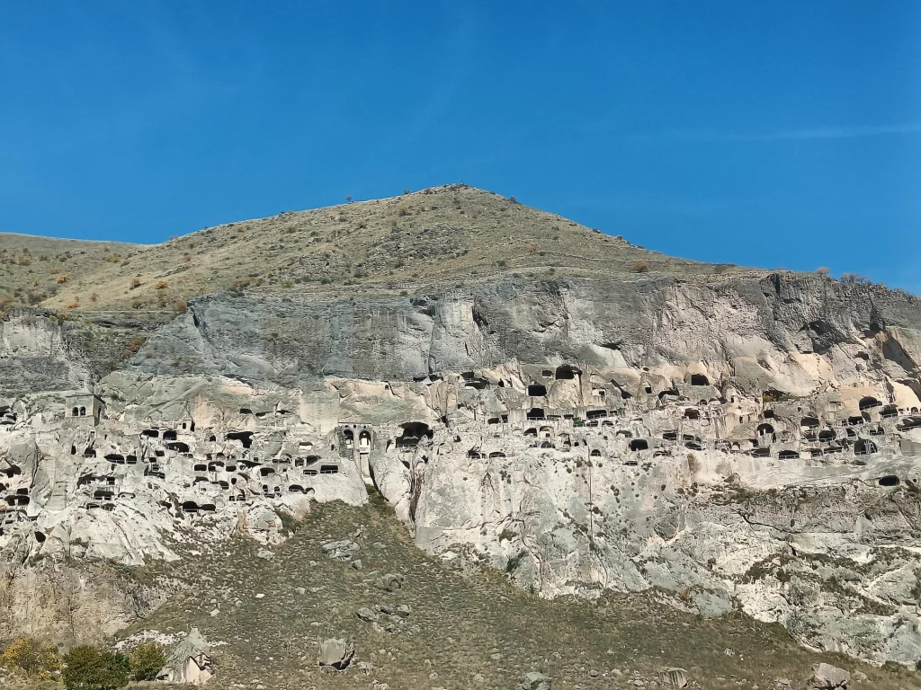 Wide daytime view of Vardzia's rock-cut cave dwellings beneath a clear blue sky.