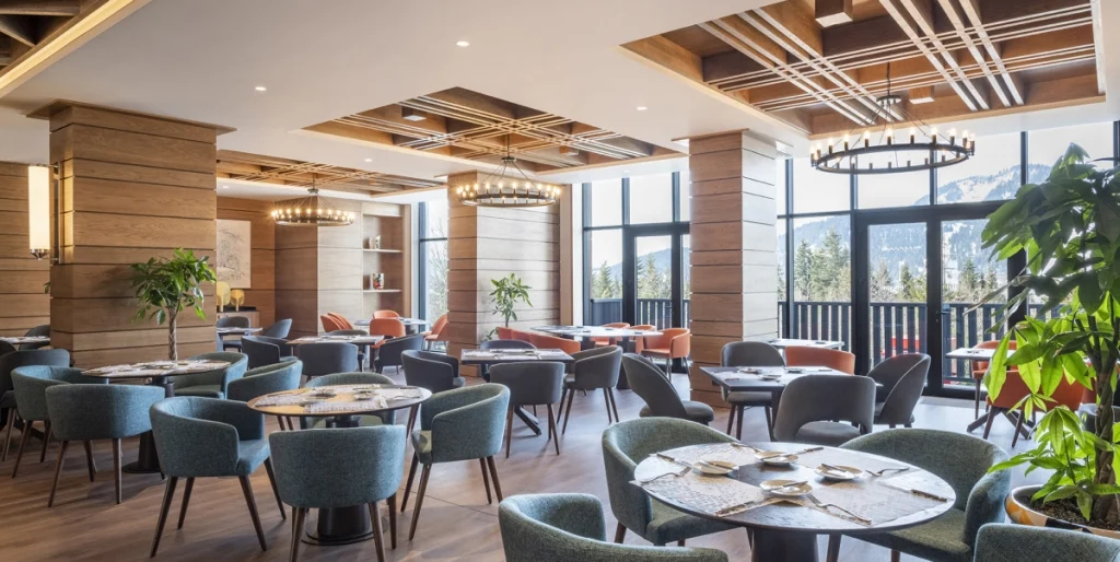 A la Carte Restaurant — Spacious restaurant with wooden ceiling, blue chairs, and large windows showing mountain views.