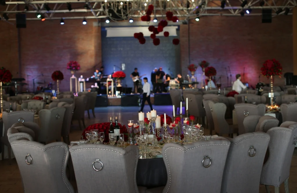 Banquet Hall — Banquet hall interior with upholstered chairs, red floral centerpieces, and a live band stage.
