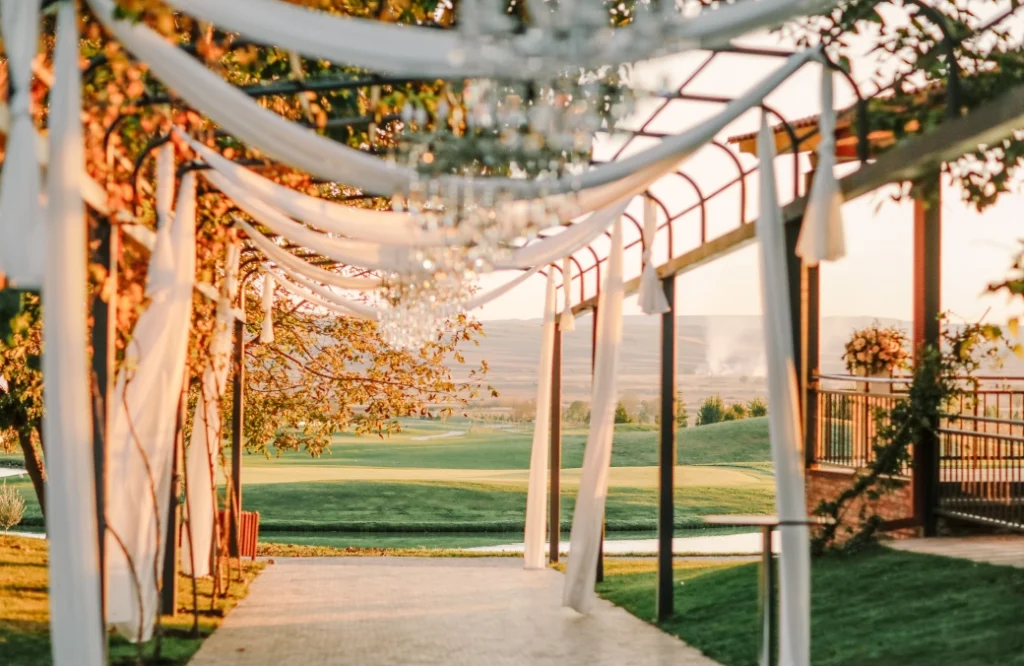 Banquet Hall — Outdoor pergola walkway with draped fabric overlooking landscaped grounds at sunset.
