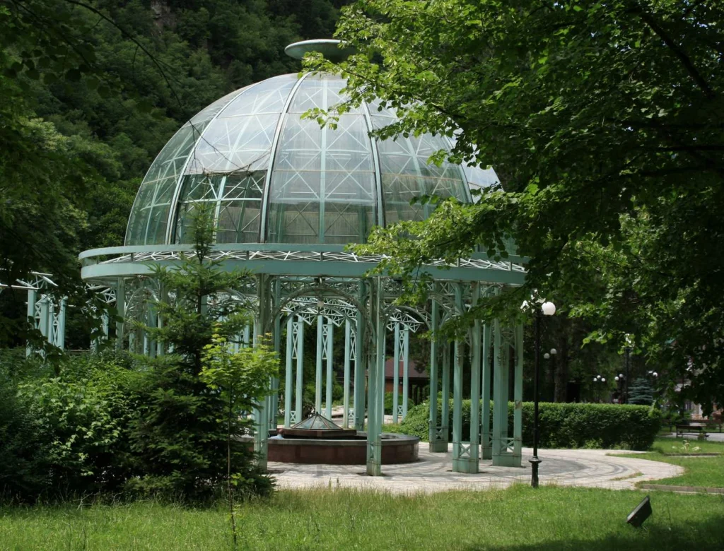 The elegant green ironwork fountain pavilion stands amid greenery in Borjomi Central Park.