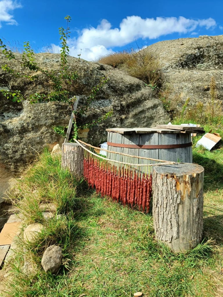 Freshly dipped churchkhela drying outdoors on a wooden rack against a rocky, blue-sky backdrop.