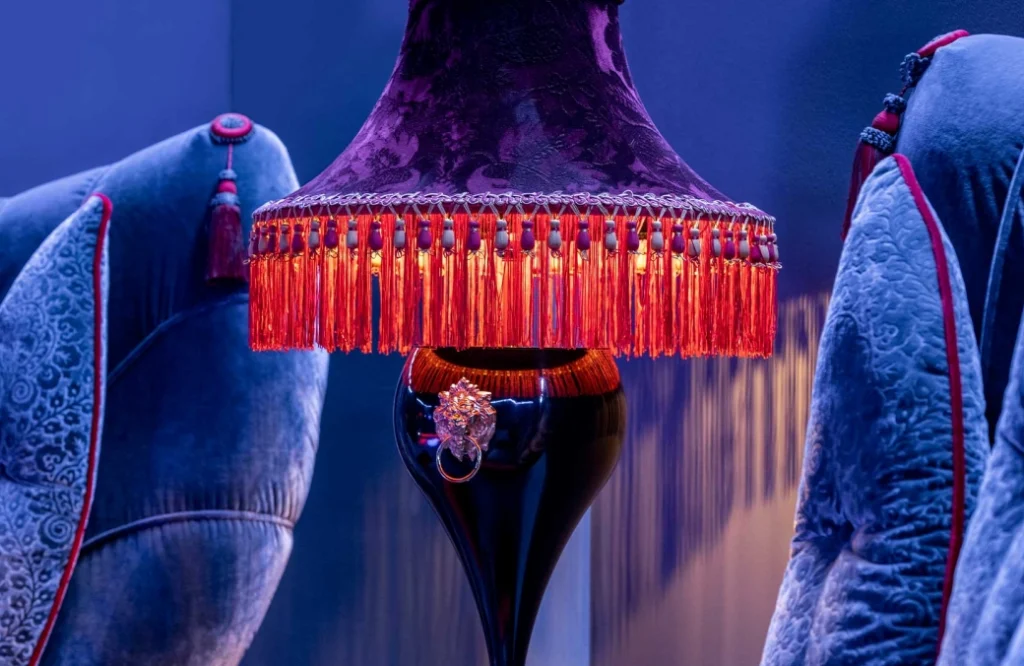 Club — Detail shot of an ornate tasseled lamp beside velvet upholstered furniture.