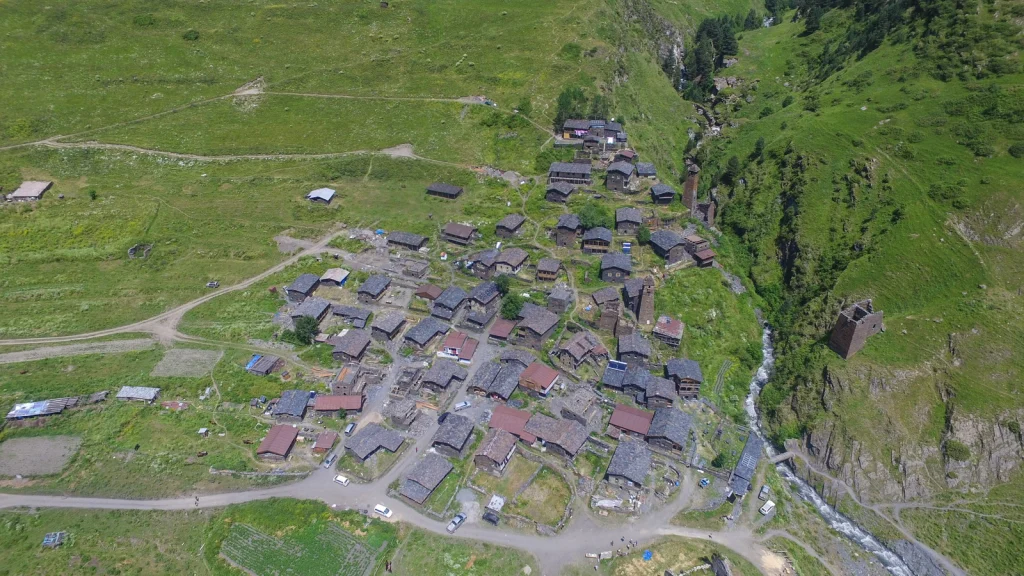 Drone shot of a Tusheti mountain village with stone towers beside a rushing river.