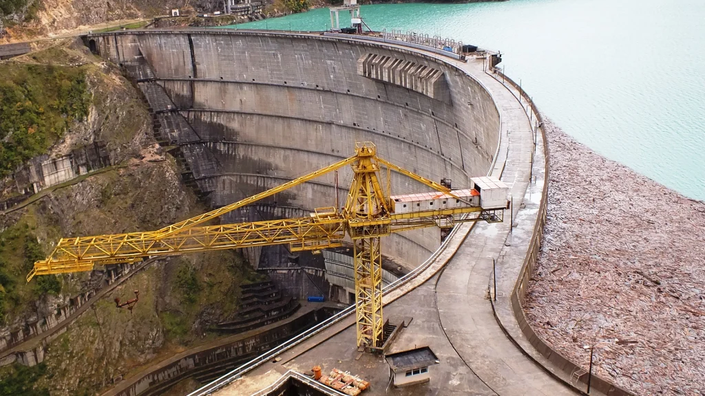 Aerial view of the curved Enguri arch dam with turquoise reservoir water and a crane.